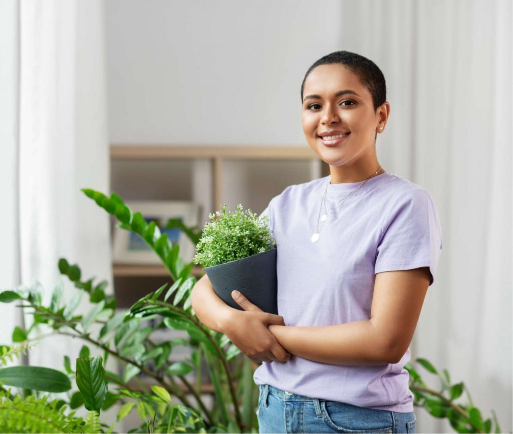 African-American women a holding plant with more plants behind — Plant Names: ZZ plant (background)